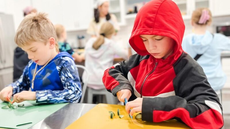 Two children practice cutting vegetables during a hands-on cooking activity at Flour Power Studios.