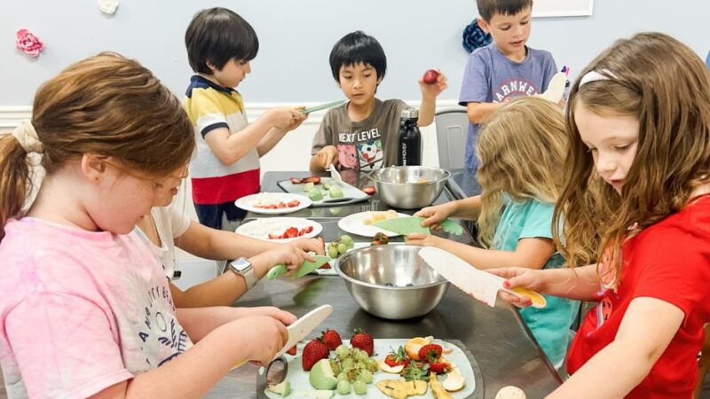 Children prepare fresh fruit together during a hands-on cooking activity at Flour Power Studios.